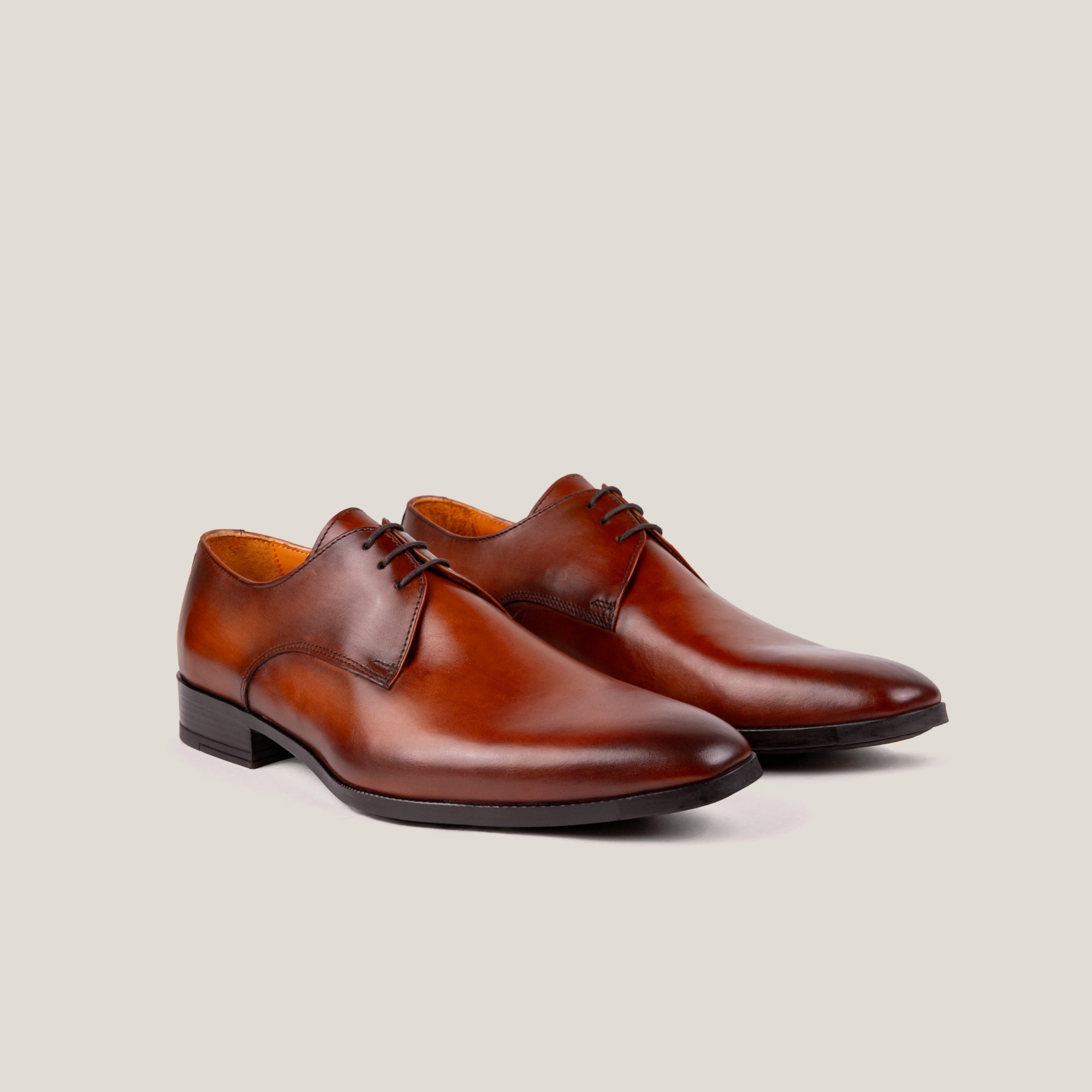 A pair of cognac brown leather Derby shoes with a plain toe and three eyelets, displayed against a white background.