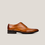 A light cognac brown leather brogue shoe with decorative stitching and a black sole.