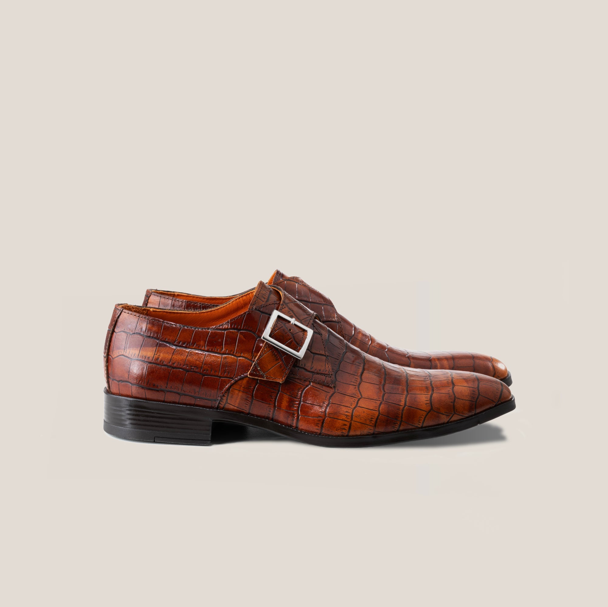 A single monkstrap shoe in light cognac brown, hand patinated on crocodile patterned leather with a square buckle.