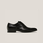 A single black leather cap toe Oxford shoe with a lace-up closure, isolated on a white background.